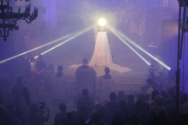 A group of people watching a priest on a stage AI-generated content may be incorrect.