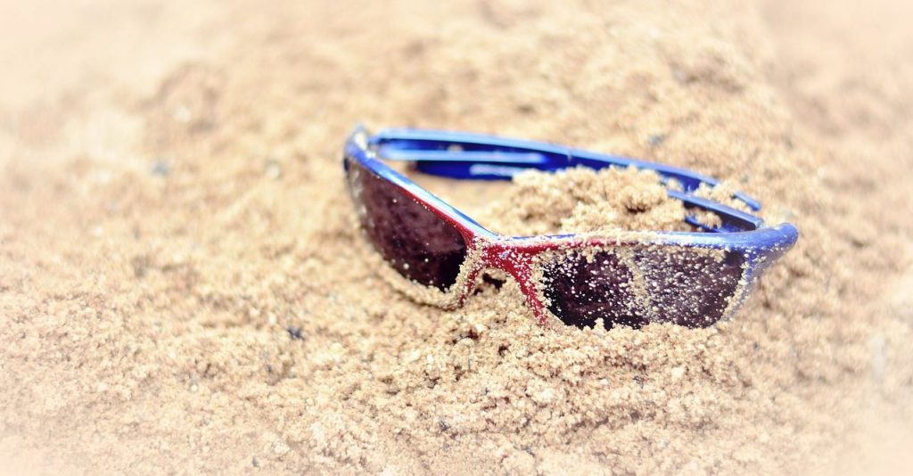 A pair of sunglasses in the sand AI-generated content may be incorrect.