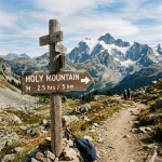 Wooden signpost showing directions and distances to Holy Mountain and trailhead in mountainous landscape